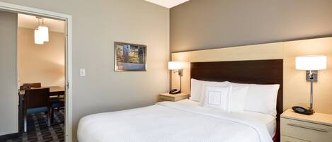 A hotel room with a large bed, bedside lamps, a desk with a chair, and a painting on the wall.