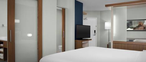 A hotel room with a large bed, a TV, a bathroom with a toilet, and a mirror.