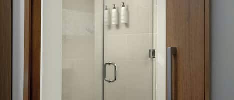 Una ducha con cerramiento de vidrio, una puerta de madera y un pomo.