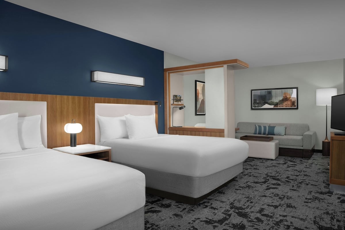 A hotel room with two beds, a sofa, a TV, a lamp, and a painting on the wall.