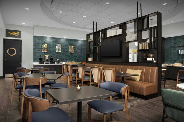 Un restaurante moderno con diversas opciones de asientos, incluyendo mesas y cabinas, una gran pantalla de televisión y una pared decorativa con fotografías enmarcadas.