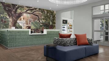 Uma área de recepção com parede estampada em verde, um sofá azul com almofadas estampadas e uma mesa lateral redonda.