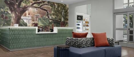 Una zona de recepción con una pared de estampado verde, un sofá azul con cojines estampados y una mesita redonda.