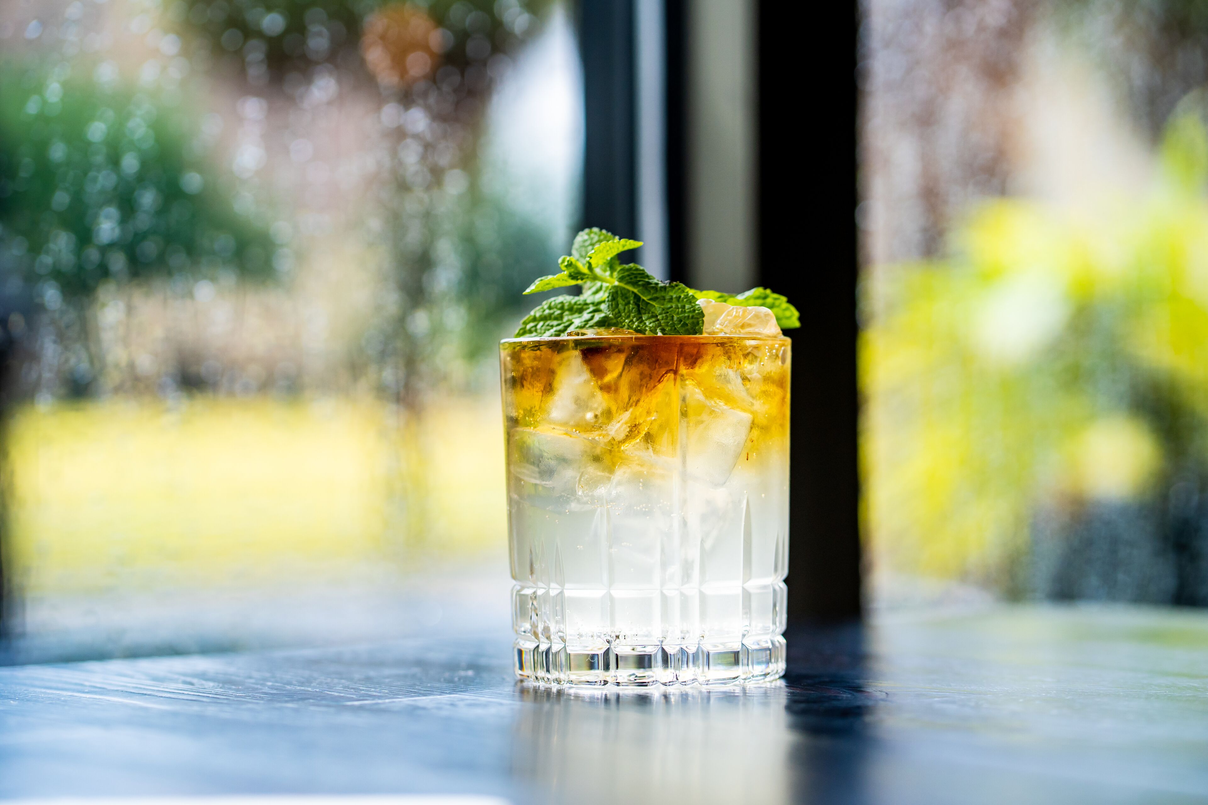 Un verre transparent contenant des glaçons et des feuilles de menthe, posé sur une surface réfléchissante.