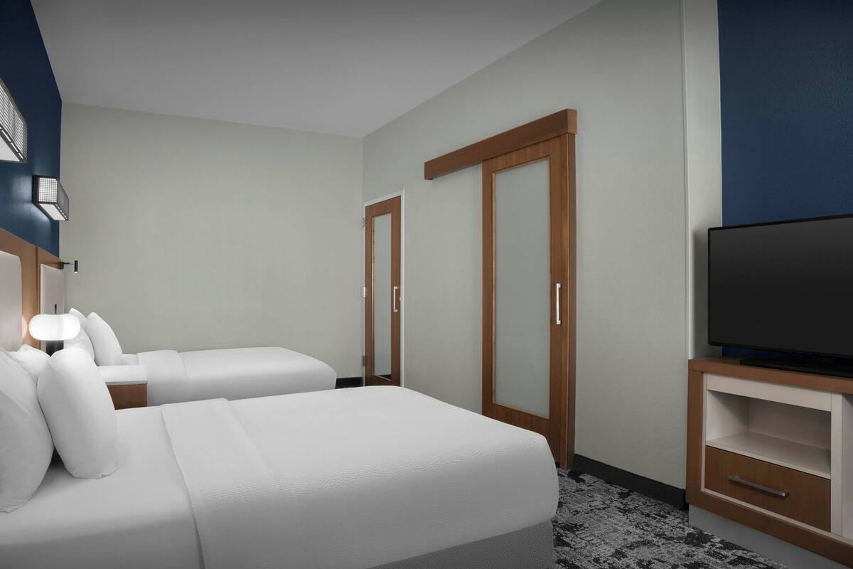 A hotel room with two beds, a TV, a wardrobe, and a bedside table with lamps.