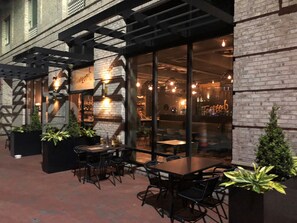 An outdoor dining area with brick walls, large windows, and potted plants. - SpringHill Suites Savannah Downtown / Historic District (Savannah)