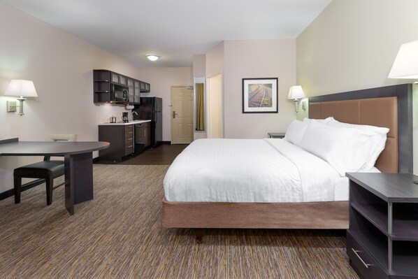 Hotelkamer met een bed, een bureau, een stoel, een kitchenette en een lijst aan de muur.
