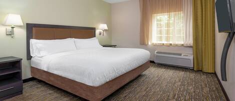 A hotel room with a large bed, two bedside lamps, a window with curtains, a wall-mounted TV, and a heater.
