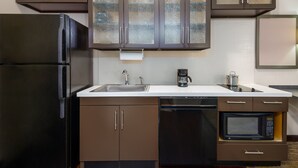 A compact kitchen with a black refrigerator, a built-in microwave, a coffee maker, and a dishwasher. - Candlewood Suites Athens by IHG (Athens)
