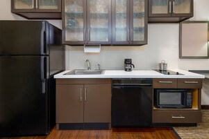 A compact kitchen with a black refrigerator, a built-in microwave, a coffee maker, and a dishwasher.