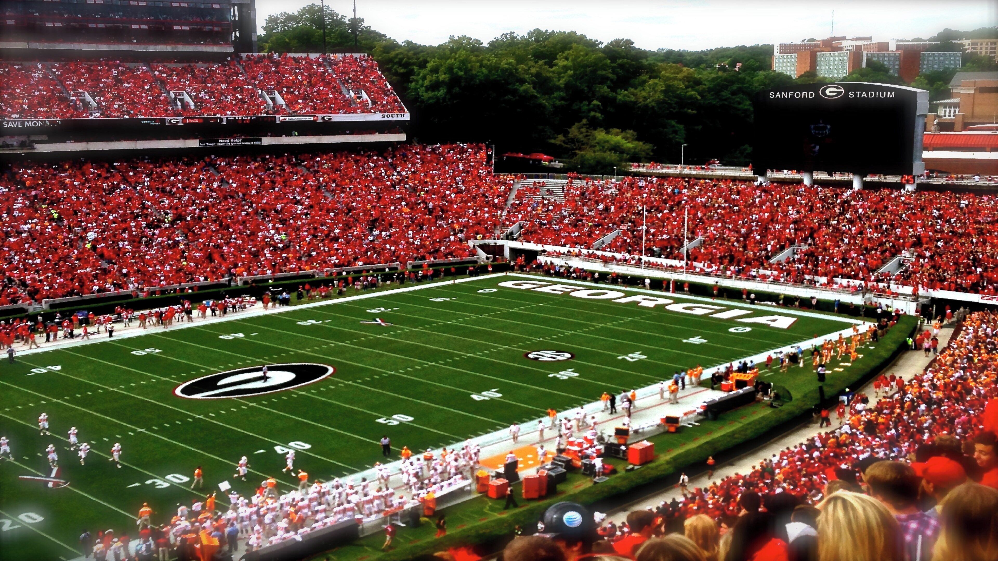 A football stadium with a large crowd, a football field, and a scoreboard.