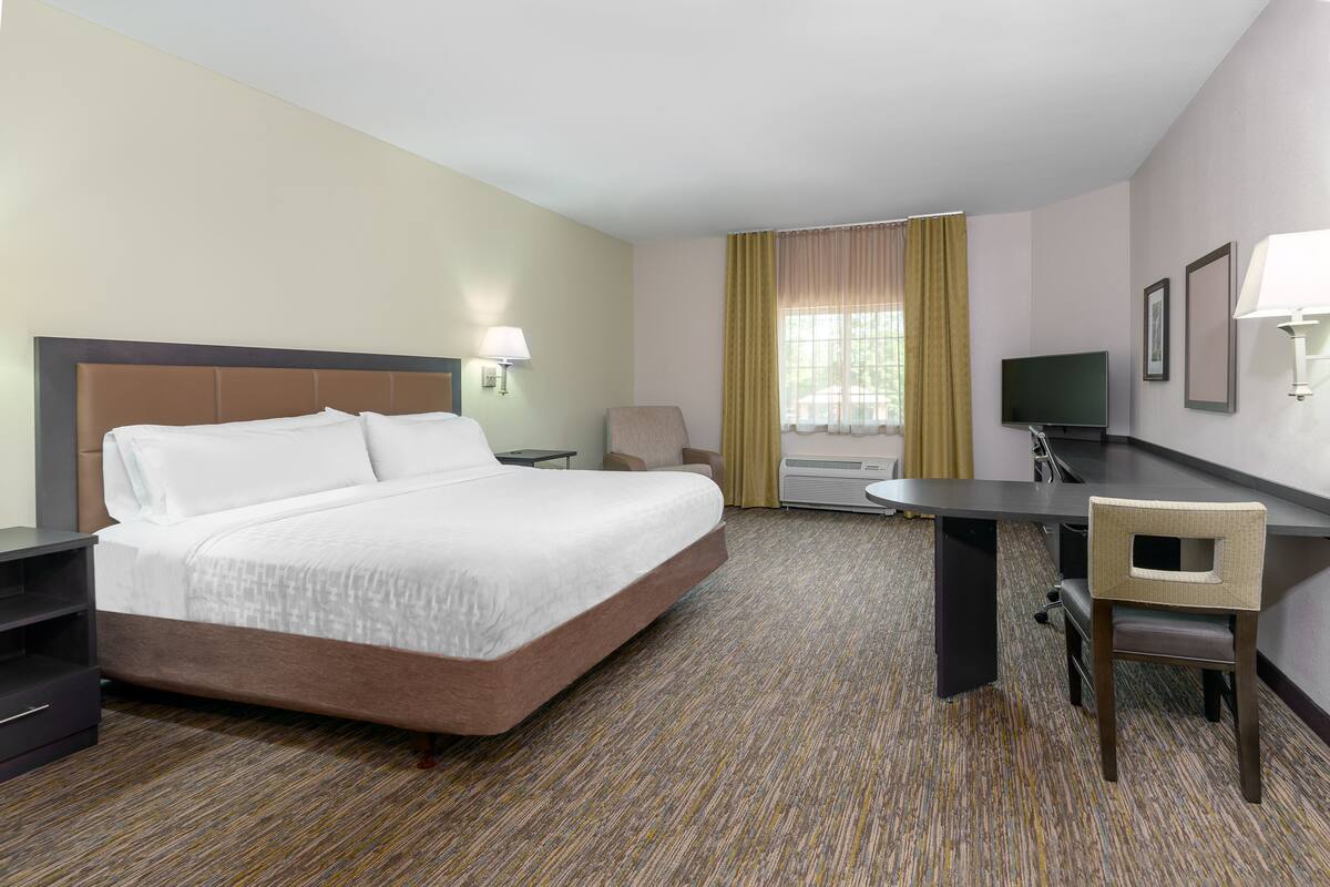 A hotel room with a large bed, a desk, a chair, a television, and a window with curtains.