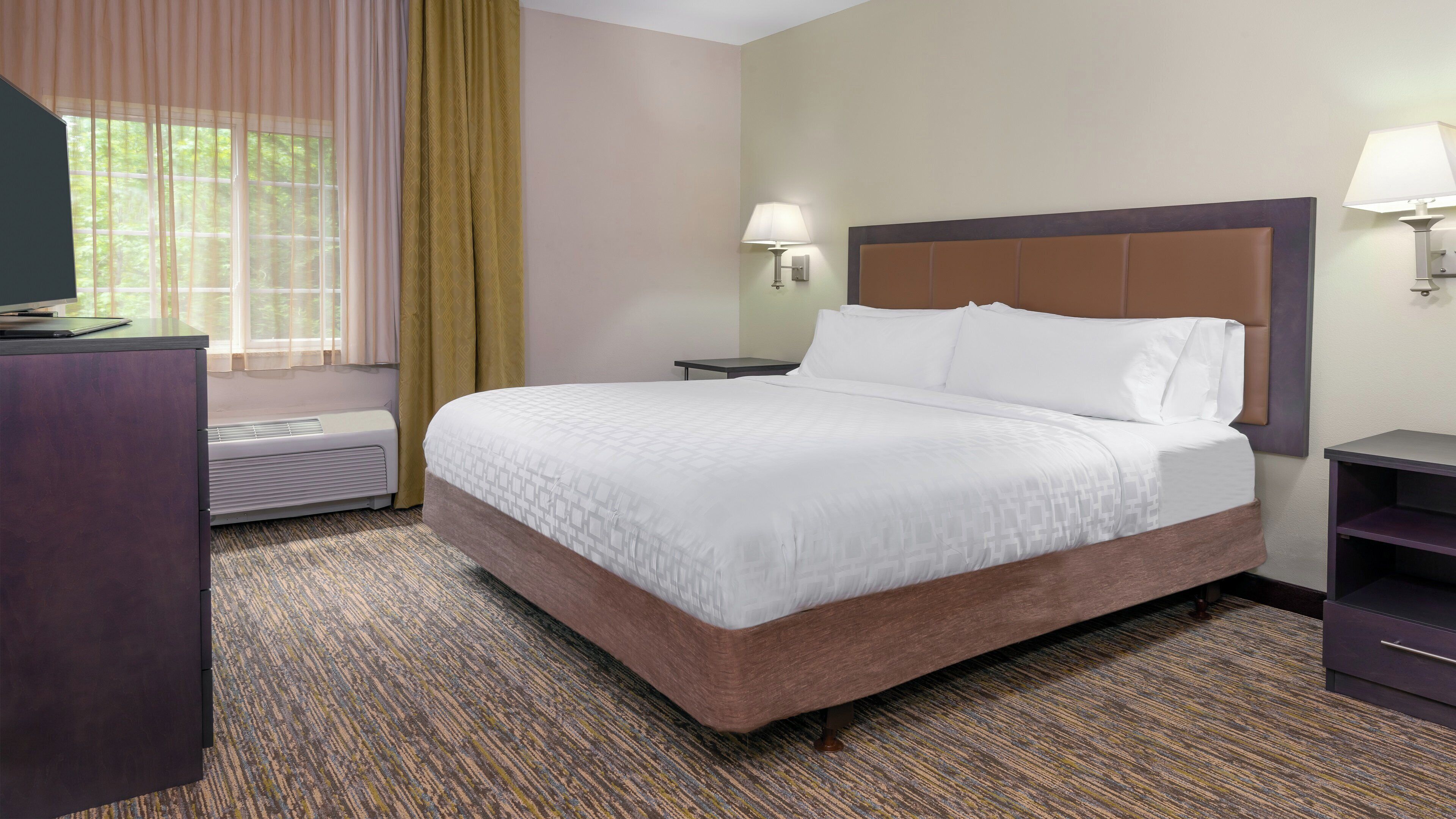 A hotel room with a bed, bedside lamps, a desk, and a window with curtains.