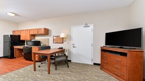 Een compacte hotelkamer met kitchenette, een eethoek, een televisie en een deur.
