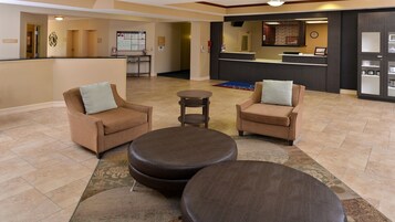 A lobby with two sofas and three ottomans, a reception desk, and a bulletin board.