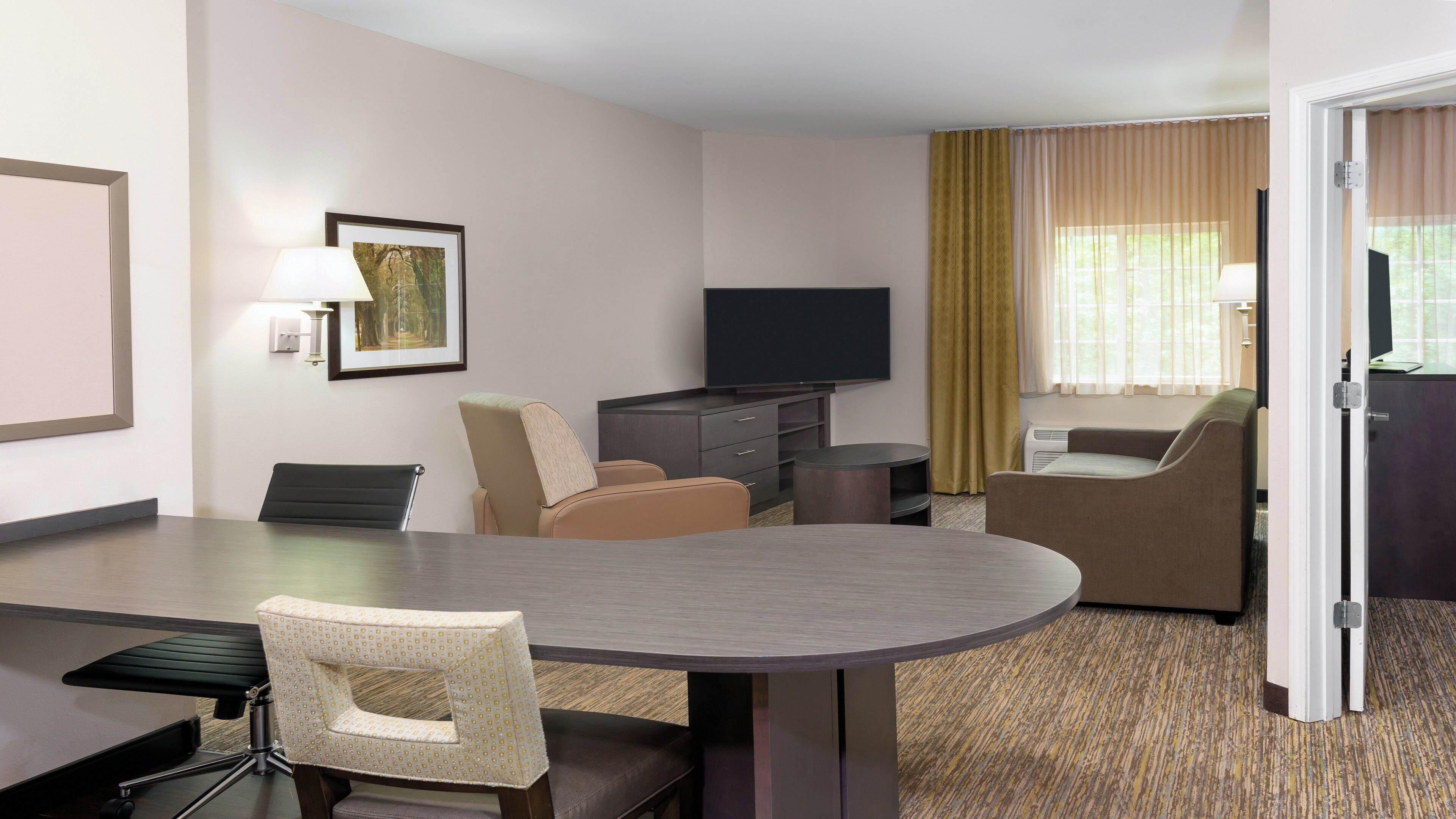 Una habitación de hotel con una mesa de comedor, dos sillas, un sofá, un televisor y una puerta.