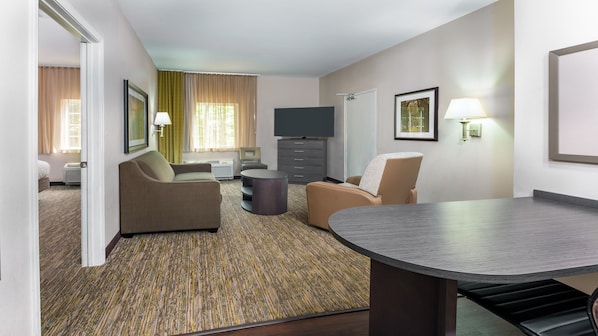 Une chambre d’hôtel équipée d’un canapé, d’un fauteuil, d’une petite table ronde et d’un téléviseur à écran plat.