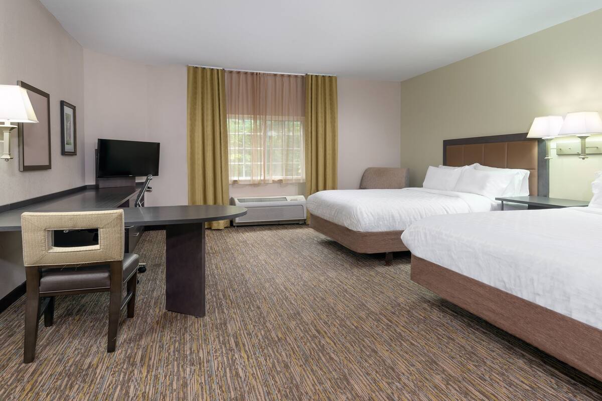 A hotel room with two beds, a desk, a chair, a TV, and a window with curtains.