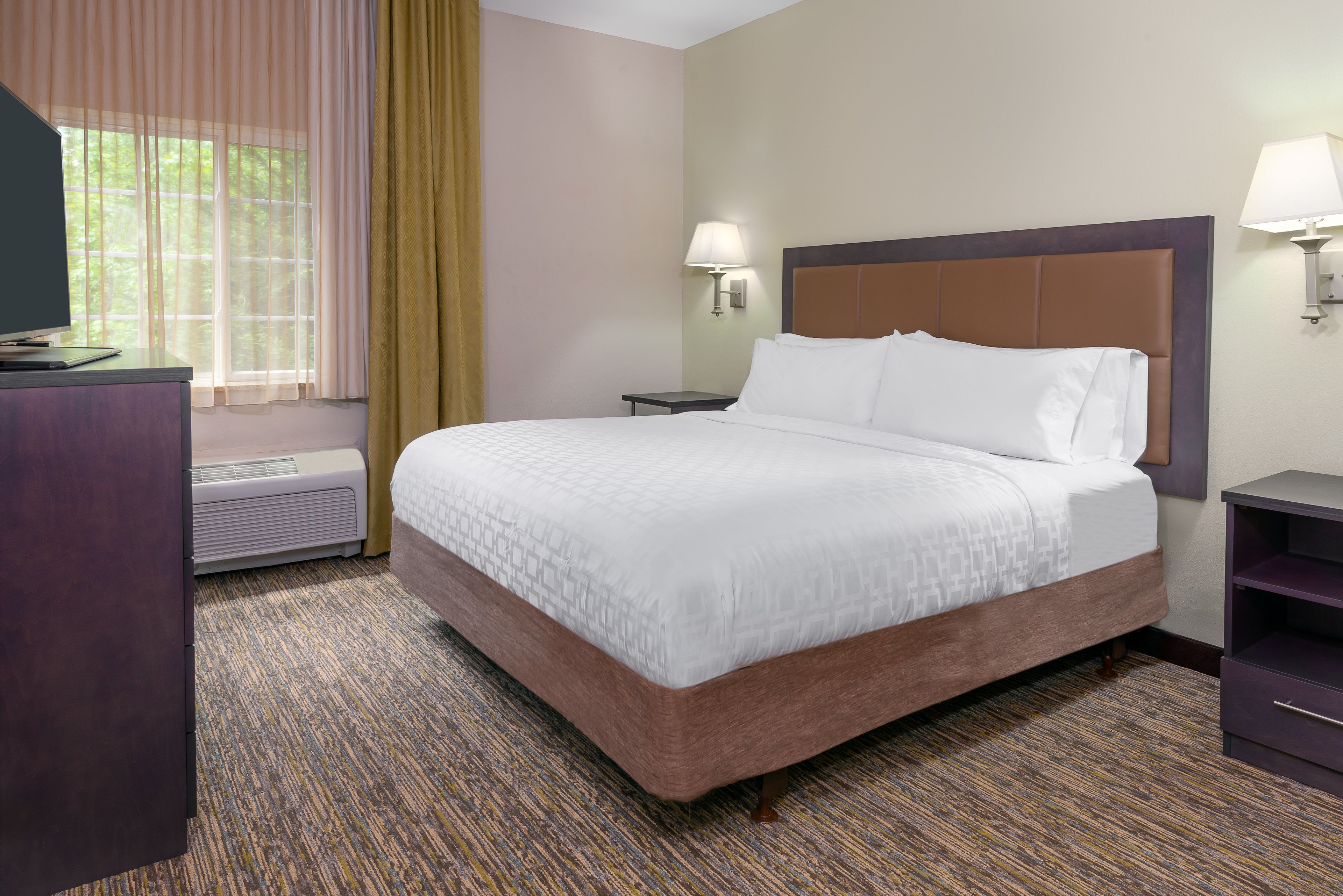 A hotel room with a large bed, a desk, a heater, and a window with curtains.