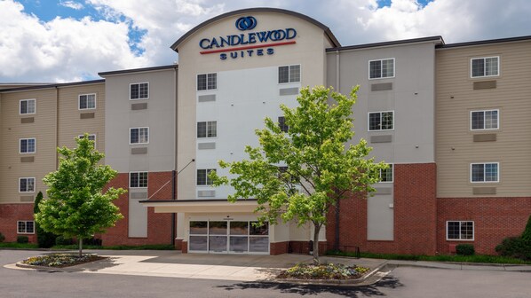 A hotel with a sign reading "Candlewood Suites". It has multiple floors, a brick facade, and a parking lot with trees. - Candlewood Suites Athens by IHG (Athens)