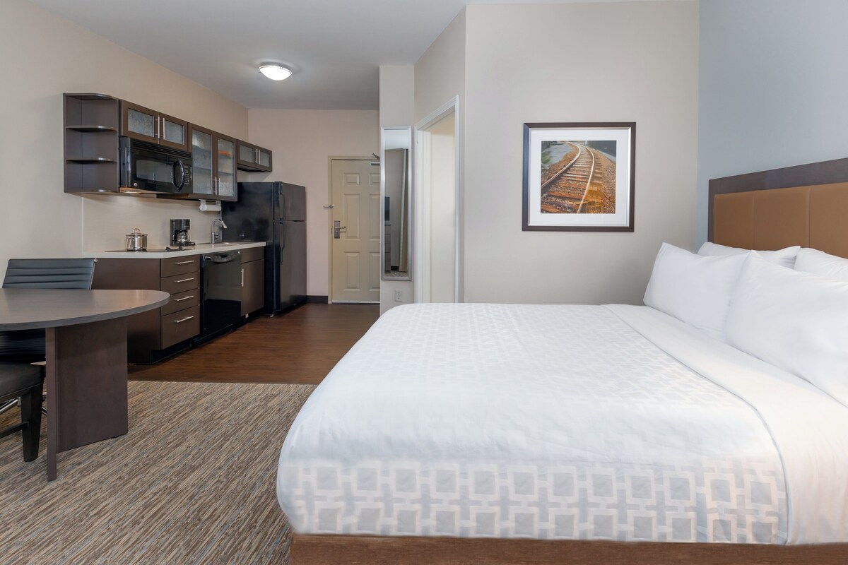 Een hotelkamer met een bed, een bureau, een kitchenette en een inlijsting foto aan de muur.