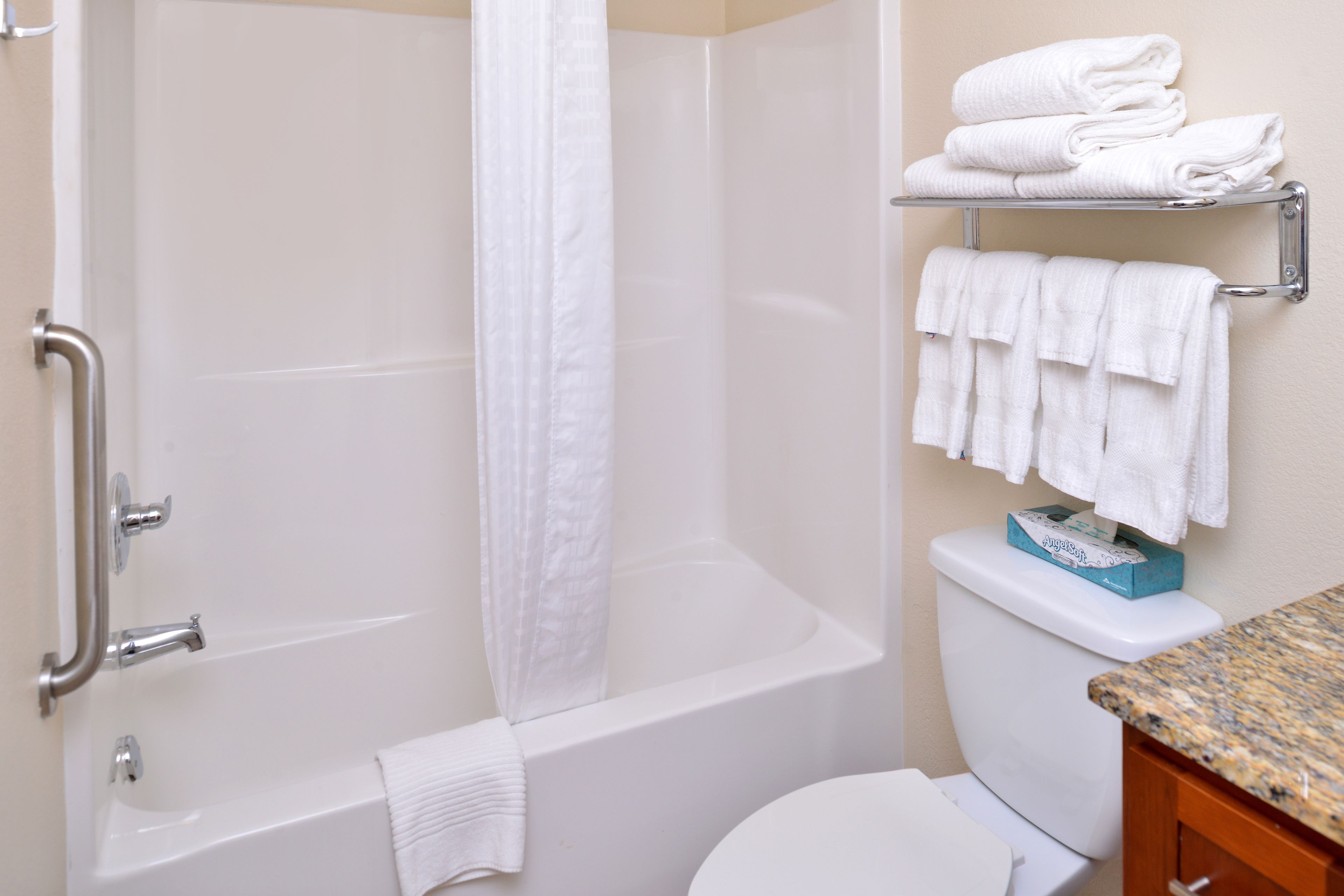 A bathroom with a white bathtub, a toilet, and a shower curtain. There are towels on a shelf and a towel hanging on the wall.