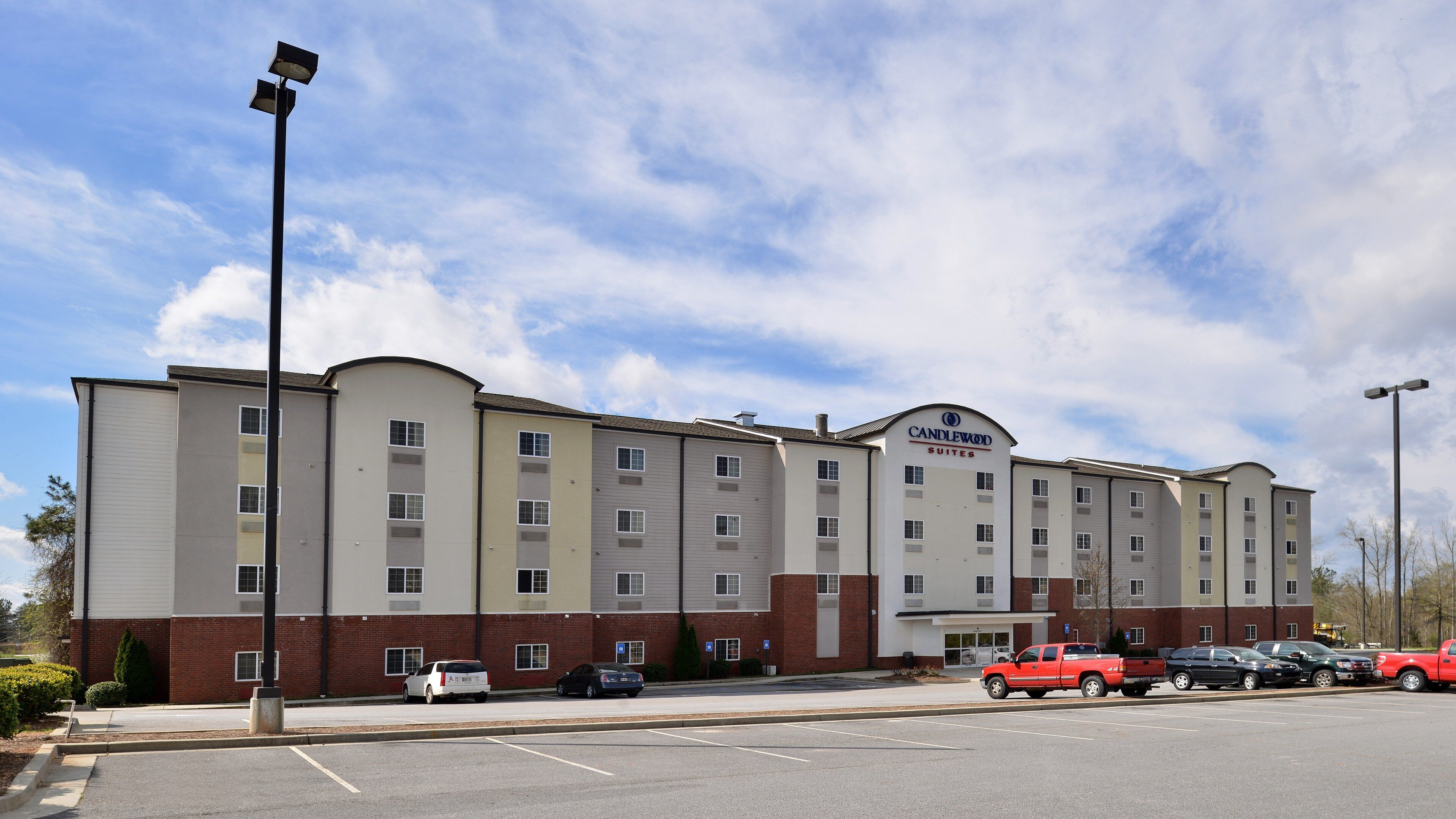 A multi-story hotel with a flat facade, a parking lot with several cars, and a clear sky.