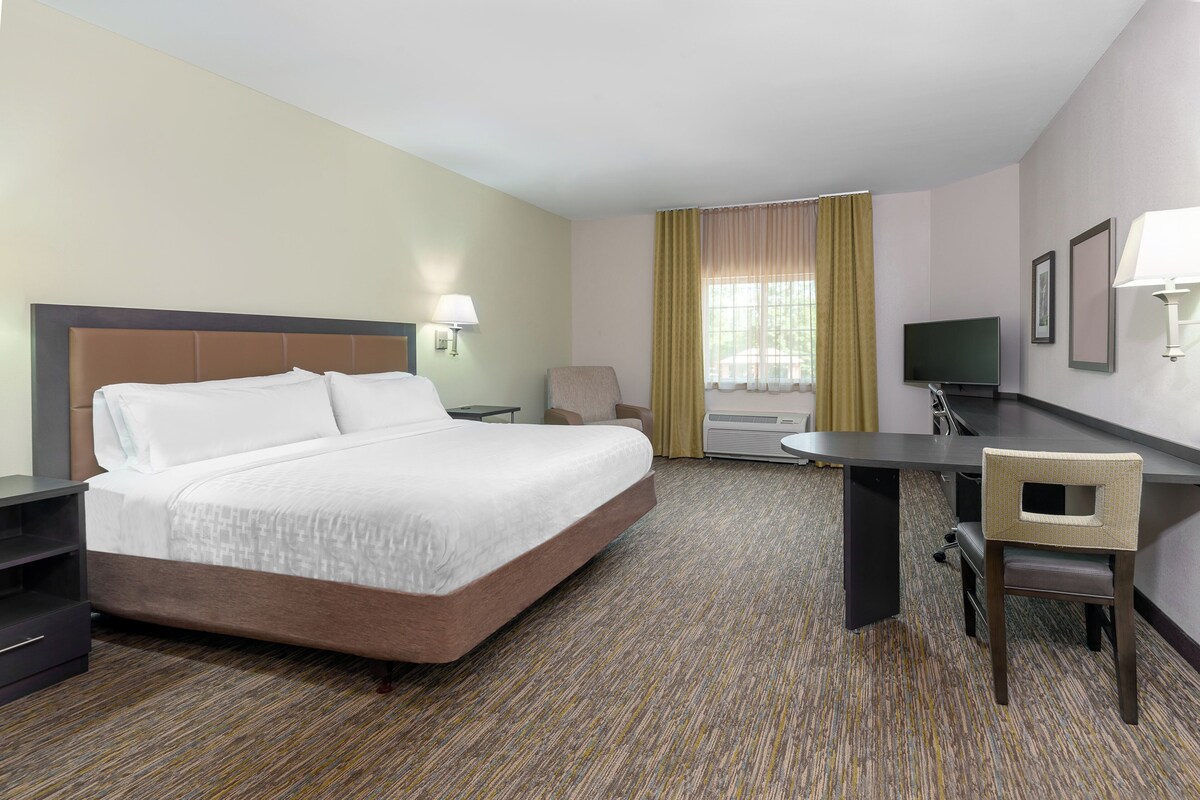 Een hotelkamer met een bed, bureau, stoel, televisie en raam met gordijnen.