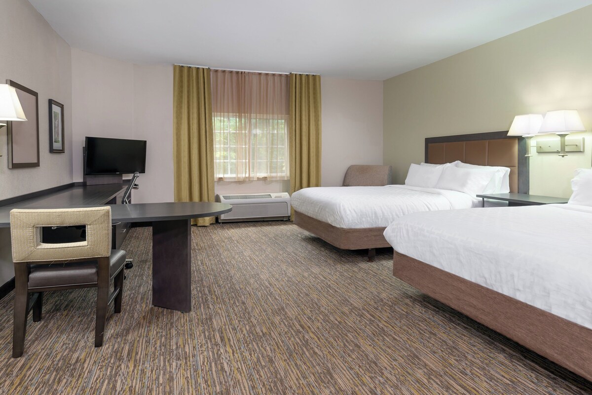 Een hotelkamer met twee bedden, een bureau, een stoel, een televisie en een raam met gordijnen.
