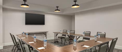 Un salón de conferencias con una larga mesa, sillas, botellas de agua e iluminación colgante.