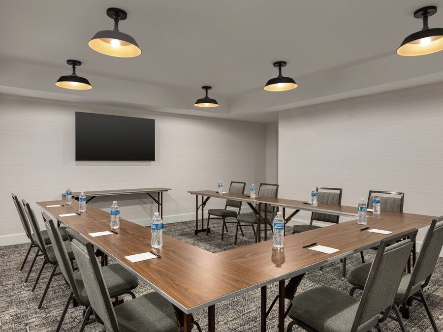 Sala de conferência com uma mesa comprida, cadeiras, garrafas de água e iluminação pendente.
