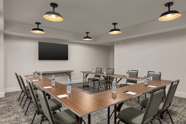 A conference room with a long table, chairs, water bottles, and pendant lighting.