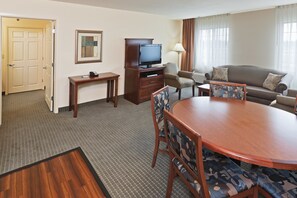 Een hotelkamer met een eettafel, stoelen, een televisie, een bank en een lamp.