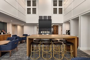 Una hall moderna di un hotel con zona bar centrale, posti a sedere e un grande schermo.