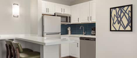 A modern kitchen with white cabinetry, stainless steel appliances, and a bar area with stools.