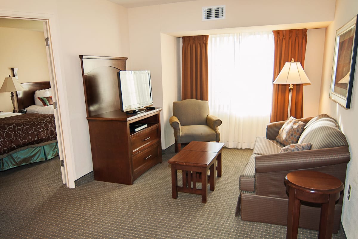 A hotel room with a bed, a desk with a television, a chair, a sofa, and a lamp.