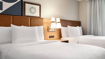 A hotel room with two beds, a headboard, bedside tables, lamps, and a framed picture on the wall.