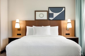 A hotel room with a large bed, two bedside lamps, a headboard, and two framed pictures on the wall.