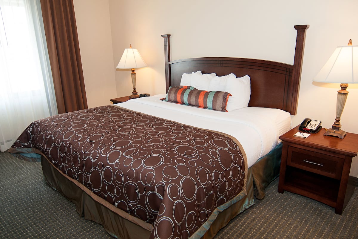 A hotel room with a large bed, two bedside tables with lamps, a nightstand, and a window with curtains.