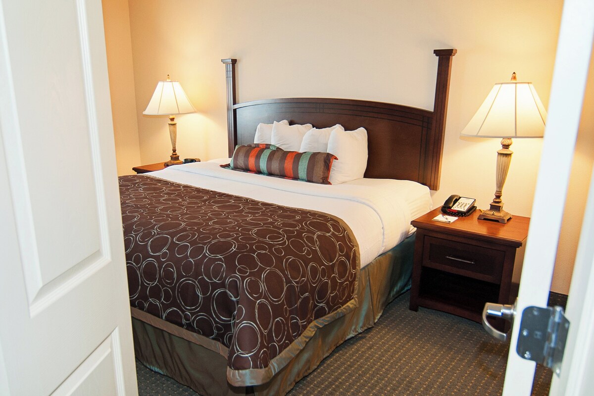 A hotel room with a large bed, two bedside tables, a nightstand, a lamp, and a telephone.