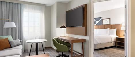 A hotel room with a desk, chair, sofa, and a bed.