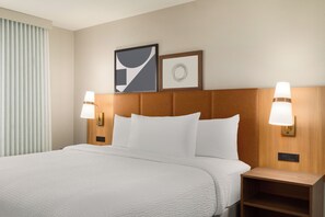 Una camera d'albergo con un letto grande, due lampade ai comodini, una testiera e due opere d'arte appese al muro.