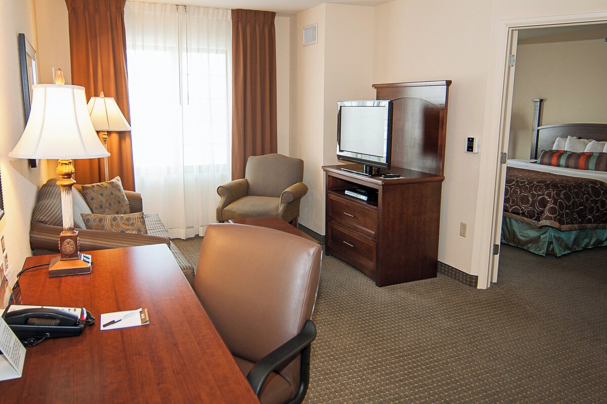 A hotel room with a desk, two lamps, a television, a chair, and a bed.