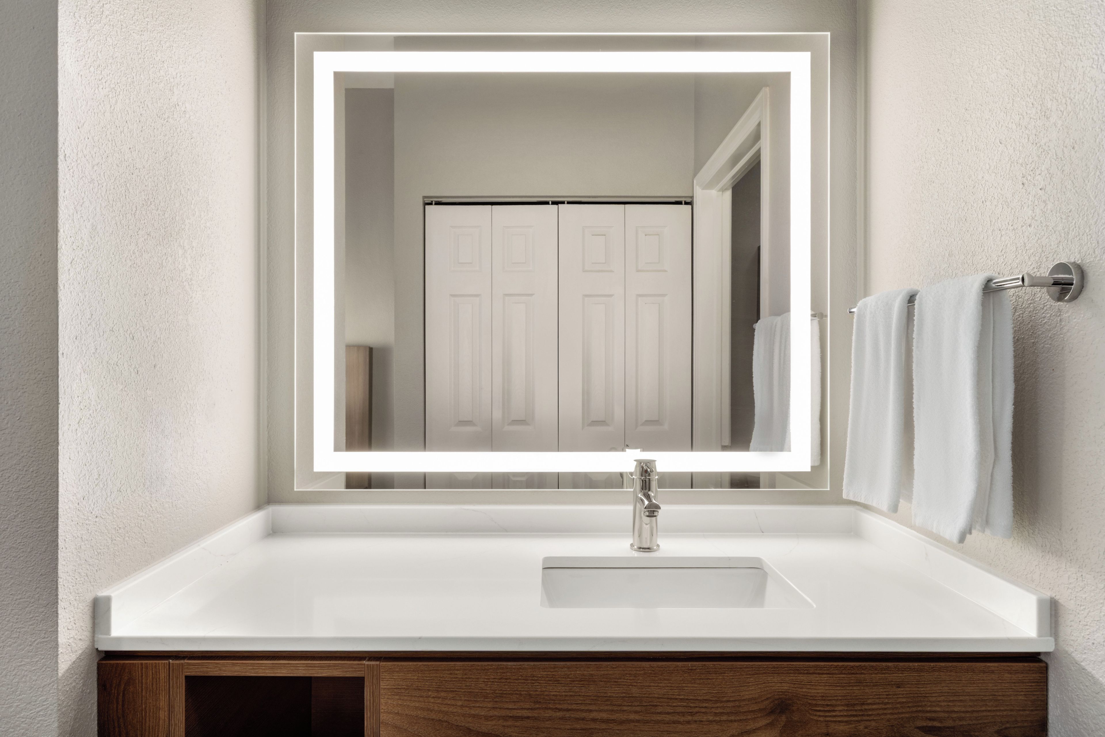 A bathroom with a white sink, a mirror with a light, a wooden cabinet, and a towel rack.