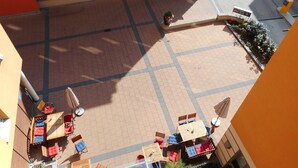 Un patio con mesas al aire libre, un coche estacionado en la calle y un edificio con un cartel.