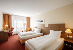 Una habitación de hotel con dos camas, un escritorio, una silla, una lámpara y una ventana con cortinas.