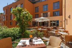 An outdoor cafe area with tables and chairs, surrounded by greenery and a building with multiple windows. - Best Western Hotel Bamberg (Bamberg)