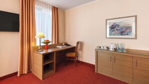 A hotel room with a wooden desk, a chair, a TV mounted on the wall, a painting, and a minibar. - Best Western Hotel Bamberg (Bamberg)