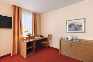 A hotel room with a wooden desk, a chair, a TV mounted on the wall, a painting, and a minibar. - Best Western Hotel Bamberg (Bamberg)
