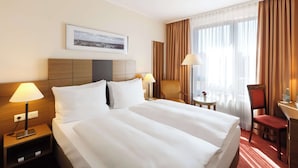 Habitación de hotel con una cama grande, dos mesitas de noche, un escritorio, una silla y una ventana con cortinas.